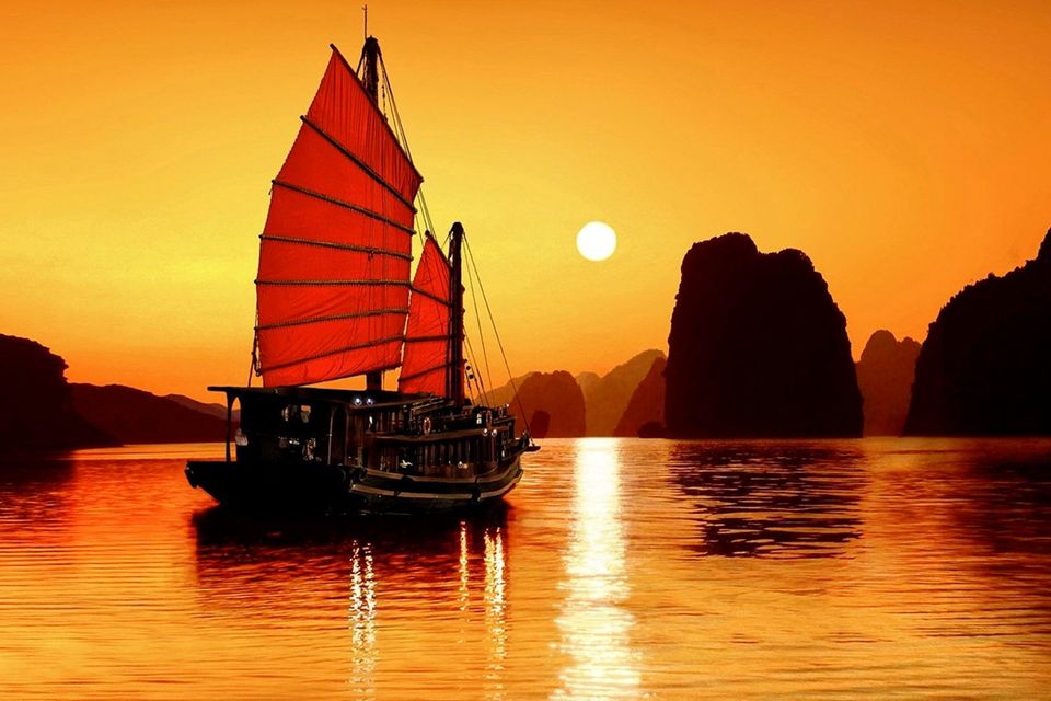Traditional luxury cruise vessel sailing past limestone karst formations in Halong Bay, Vietnam