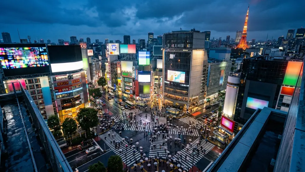 Shibuya Crossing in Tokyo at twilight with illuminated buildings, pedestrians, and Tokyo Tower visible in the distance, representing modern urban Japan.